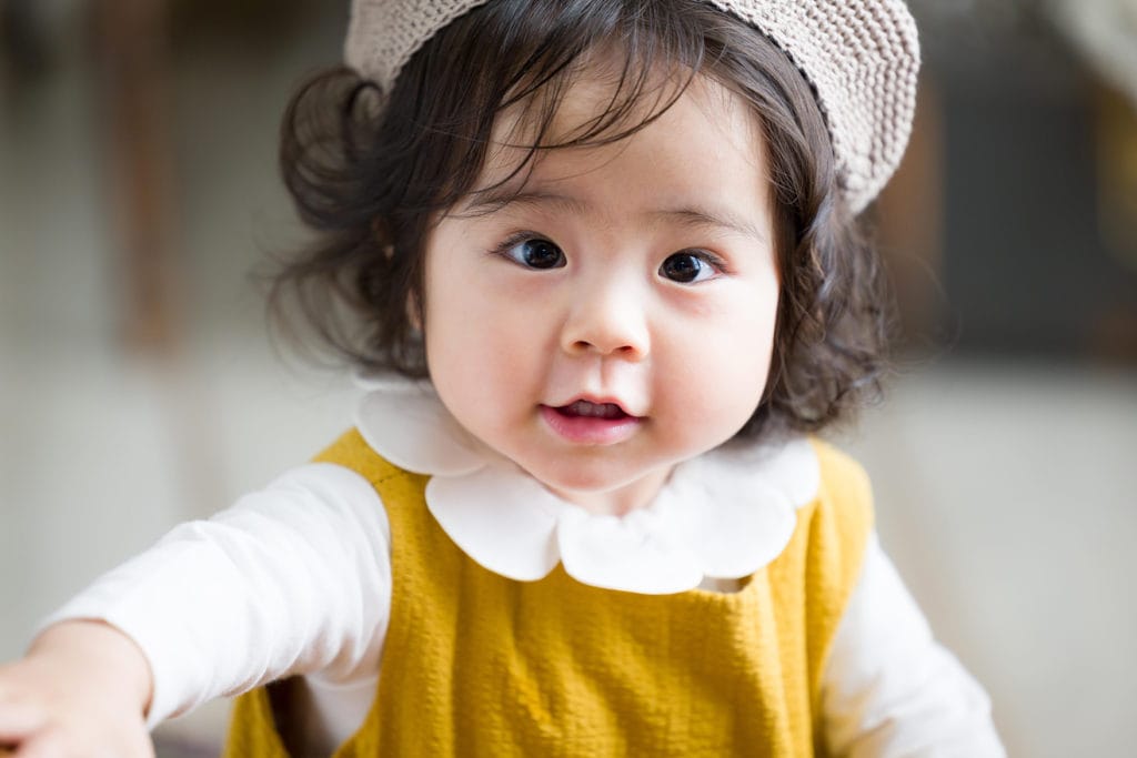 にっこり笑顔の1歳の赤ちゃん、柔らかな自然光が差し込むアンティーク風スタジオで撮影